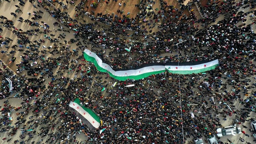 An aerial picture shows Syrians waving the national flag during a gathering in the rebel-held city of Idlib on March 15, 2021, as they mark ten years since the nationwide anti-government protests that sparked the country's devastating civil war. Credit: AFP Photo