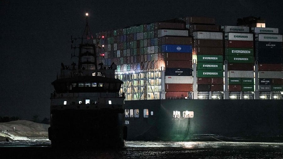 This picture taken late on March 27, 2021 shows a view of tugboats by the Panama-flagged MV 'Ever Given' container ship, which has been wedged diagonally across the span of the canal about six kilometres north of the Suez Canal's entrance by the Red Sea port city of Suez since March 23. Credit: AFP.