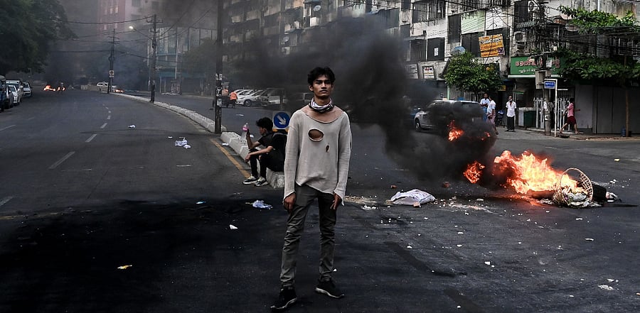 A protester stands near a burning makeshift barricade during a protest against the military coup, in Yangon. Credit: AFP Photo