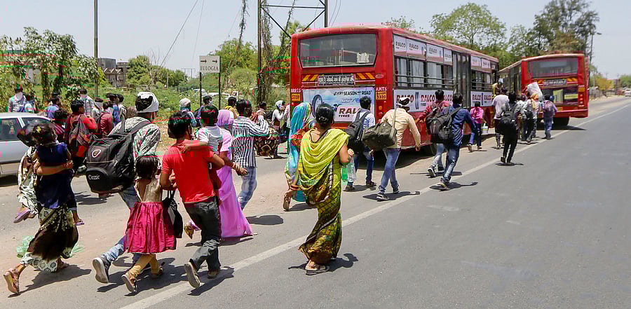 Migrant workers run to catch a bus for the railway station to return to their homes in Ahmedabad. Credit: PTI Photo