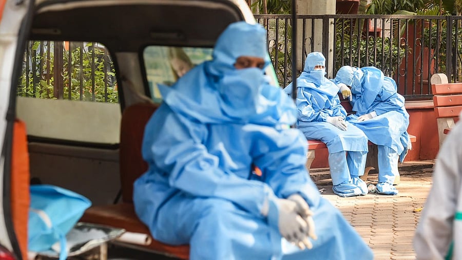 Family members, wearing PPE kits, wait during cremation of a COVID-19 victim, at the Nigambodh Ghat in New Delhi. Credit: PTI Photo
