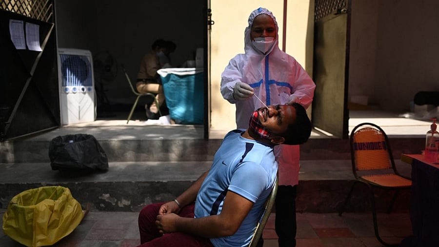 A health worker takes a swab sample from a man for a Reverse Transcription Polymerase Chain Reaction (RT-PCR) test, at a testing centre in New Delhi. Credit: AFP photo. 