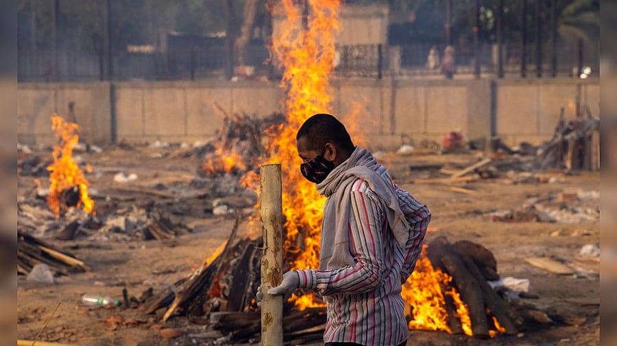 A man walks past burning funeral pyres of people, who died due to the coronavirus disease (Covid-19), at a crematorium ground in New Delhi. Credit: Reuters Photo