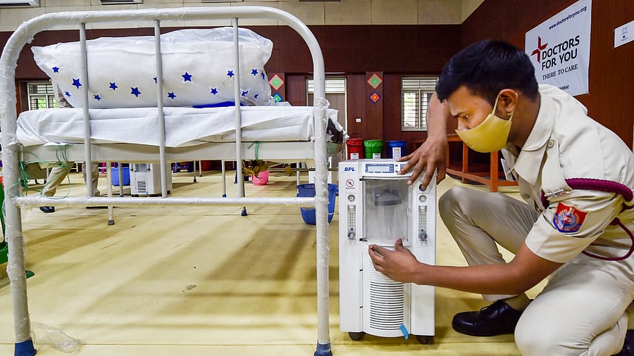 A volunteer prepares beds with oxygen concentrators and oxygen cylinders at a Covid Care Centre. Credit: PTI Photo