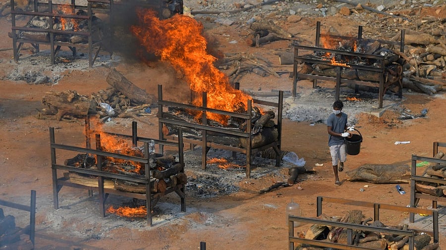 An undertaker walks amidst burning pyres of the victims who died of Covid-19 coronavirus at an open air crematorium set up for the coronavirus victims inside a defunct granite quarry on the outskirts of Bangalore on May 1, 2021. Credit: AFP Photo