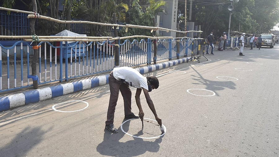 worker draws markers on the road to ensure social distancing as coronavirus cases spike across the country, outside Netaji Indoor Stadium on the eve of counting day of West Bengal Assembly Poll, in Kolkata, Saturday, May 1, 2021. Credit: PTI Photo
