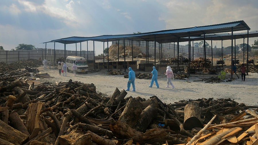 Family members and relatives wearing protective gear arrive to cremate the bodies of victims who died of Covid-19 at an open air crematorium set up for the coronavirus victims inside a defunct granite quarry on the outskirts of Bengaluru. Credit: AFP Photo
