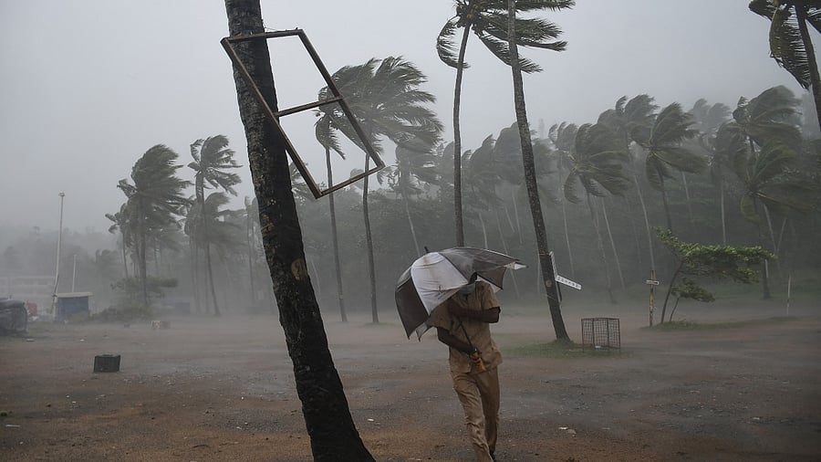 A man takes cover under an umbrella from strong wind and heavy rain, at the Kovalam coast in Thiruvananthapuram. Credit: PTI Photo