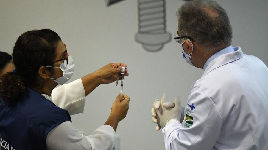 A nurse prepares a dose of a Covid-19 vaccine next to Brazil's Health Minister Marcelo Queiroga (R). Credit: AFP Photo