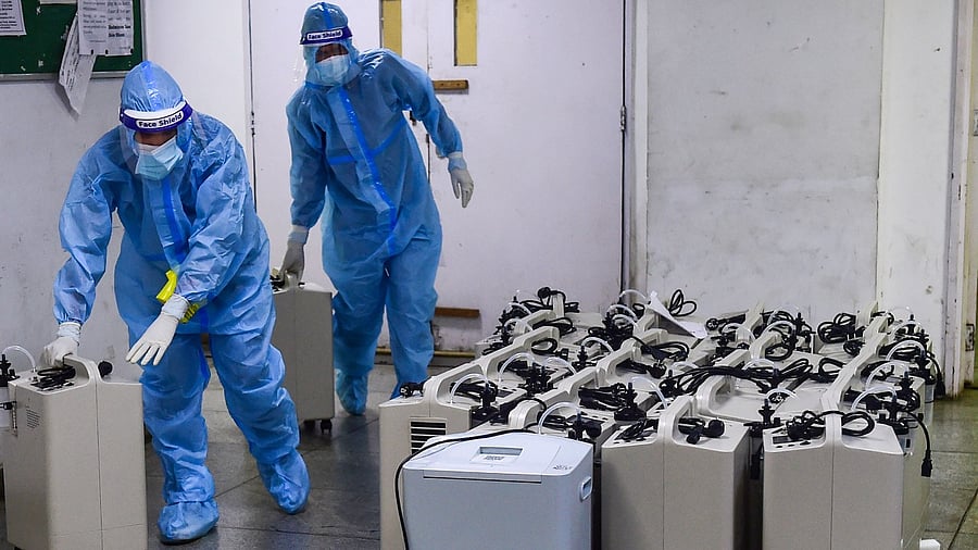Health workers wearing PPE kits arrange oxygen concentrators at Yamuna Sports Complex Covid care centre, in New Delhi. Credit: PTI File Photo
