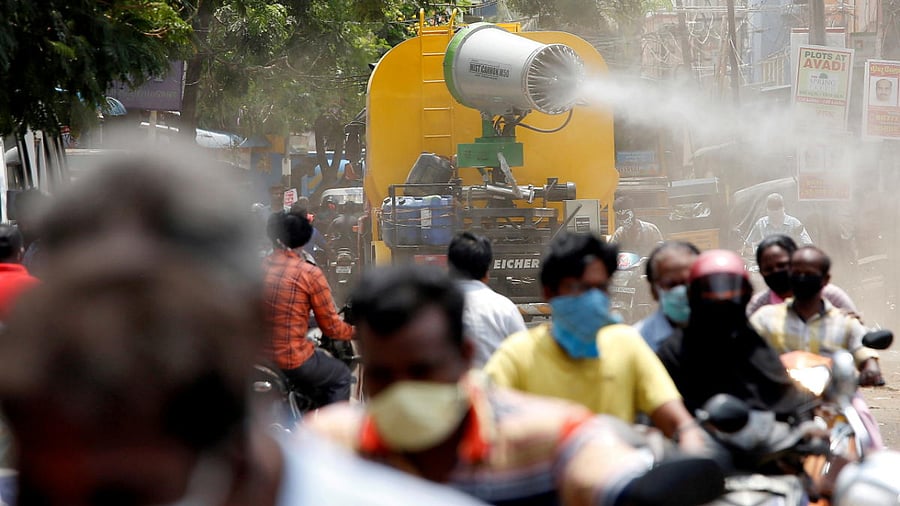 People wearing face maks ride motorcycles as a municipal vehicle decontaminates a road. Credit: Reuters File Photo