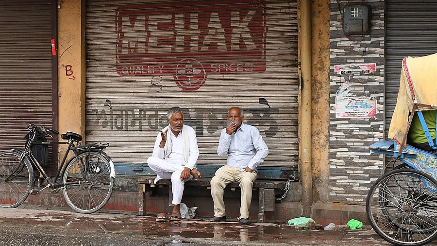 People sit outside a closed shop during weekend lockdown in Amritsar. Credit: AFP Photo