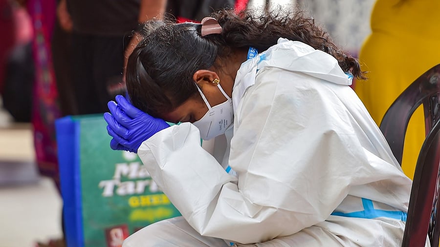 A health worker rests in between breaks from testing passengers for Covid-19, at city railway station in Bengaluru. Credit: PTI Photo