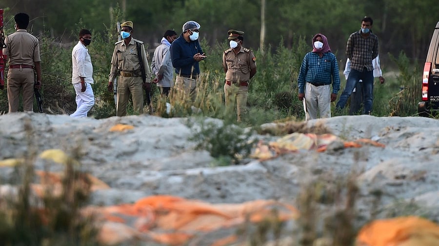 Police and administrative officials (background) inspect a cremation ground on the banks of Ganges River, where suspected bodies (foreground) of Covid-19 coronavirus victims appeared partially buried, at Rautapur Ganga Ghat in Unnao on May 13, 2021. Credit: AFP Photo