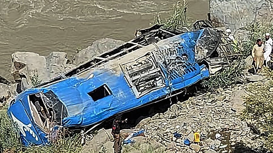 People stand next to a wreck after a bus plunged into a ravine following a bomb attack, which killed 12 people including 9 Chinese workers. Credit: AFP Photo