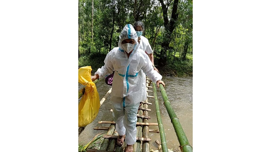 Health workers walk on a temporary bamboo bridge amidst heavy rain to reach Kalmakar village in Idyadka area of Sullia taluk, Dakshina Kannada district, for collecting swab samples to conduct Covid tests. Credit: DH photo