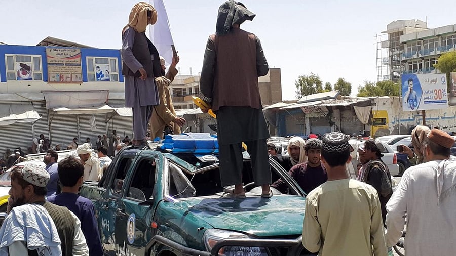 Taliban fighters stand over a damaged police vehicle along the roadside in Kandahar. Credit: AFP Photo