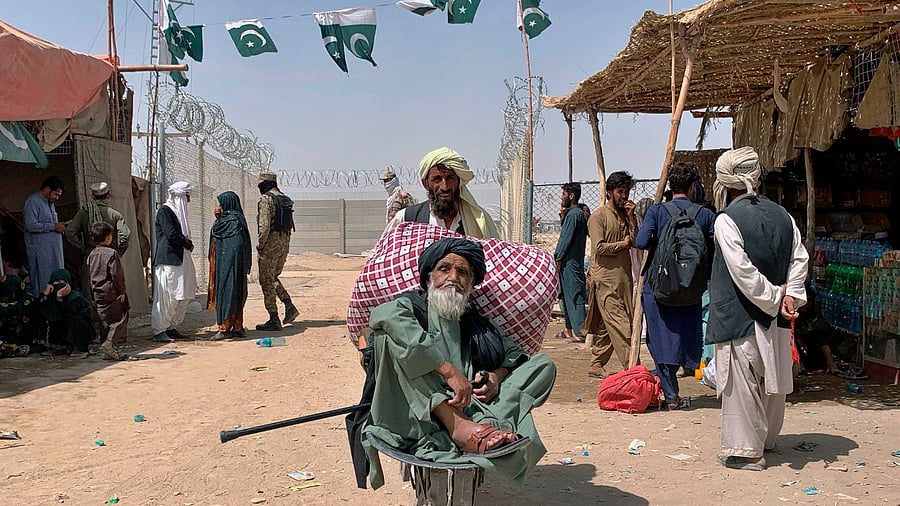 A porter pushes a wheelbarrow carrying an elderly Afghan man as he enters into Pakistan through a border crossing point. Credit: AP/PTI Photo