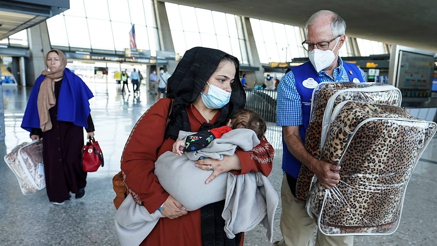An Afghan woman holding a child walks to a bus taking them to a refugee processing center upon arrival at Dulles International Airport in Dulles, Virginia August 25, 2021. Credit: Reuters Photo