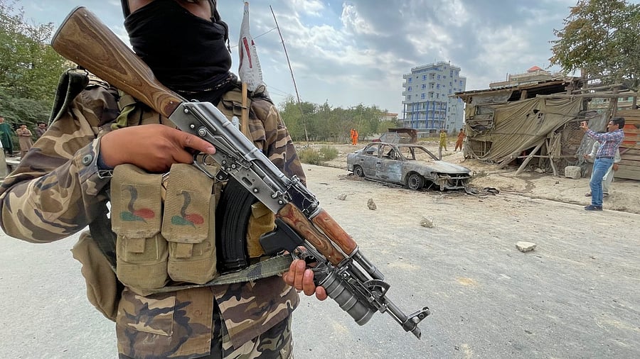 A member of Taliban forces stands guard as Afghan men take pictures of a vehicle from which rockets were fired, in Kabul. Credit: Reuters Photo