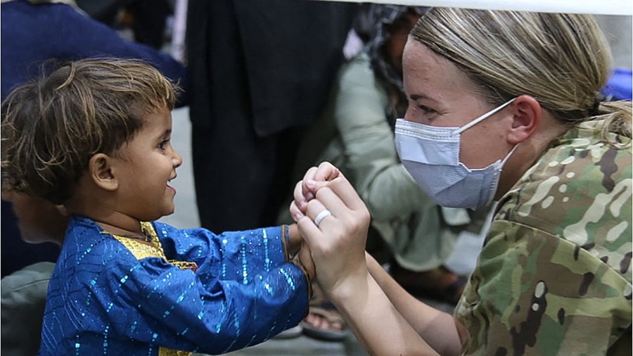 This handout photo courtesy ot the US Army shows a US Army National Guard Soldier assigned to Task Force Spartan, US Army Central, give a joyful welcome to an Afghan evacuee child during the arrival process at Camp Buehring, Kuwait, August 25, 2021. Credit: AFP File Photo