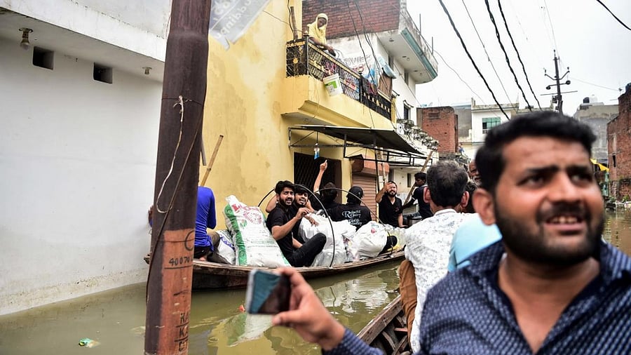 Social workers distribute food on a boat along a flooded neighbourhood in Kareli Gaus Nagar area of Allahabad on August 12, 2021 following heavy monsoon rainfalls that caused the overflowing of the Ganges and Yamuna Rivers. Credit: AFP Photo