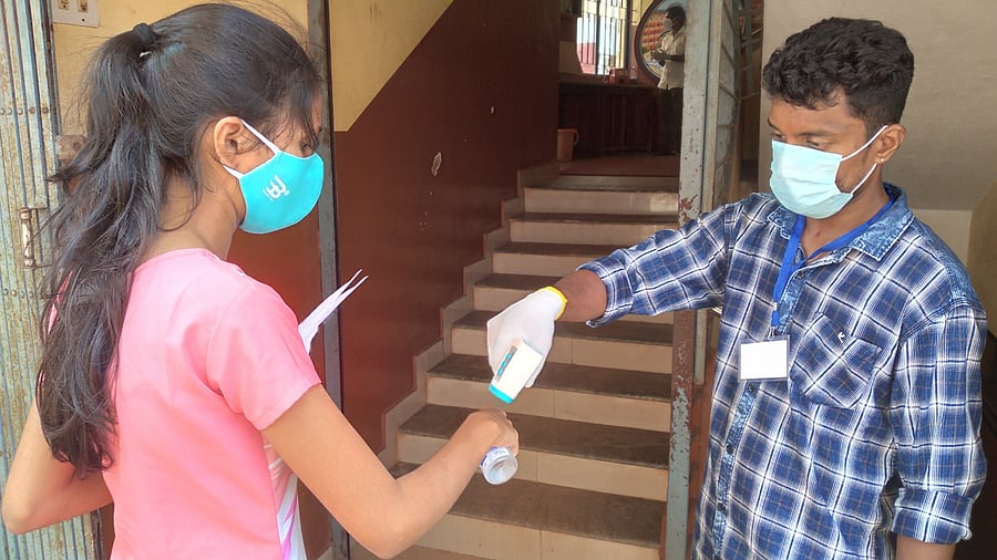 A student is being screened for body temperature before entering the classroom for NEET, in a centre in Mangaluru. Credit: DH Photo