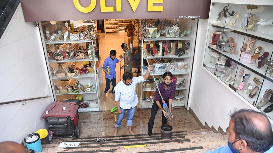 Shopkeepers at Commercial Street clean up their waterlogged premises on Monday following a heavy downpour on Sunday. DH Photo/B H Shivakumar