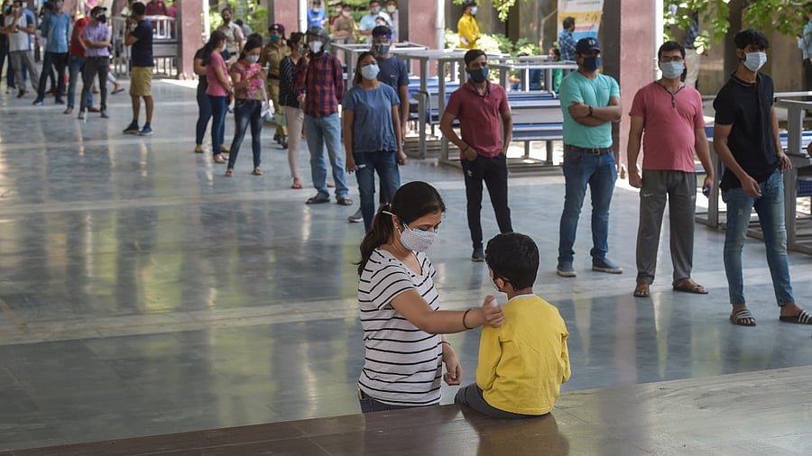 A mother reassures her child as she prepares to join a queue of people to receive first dose of COVID-19 vaccine, at a vaccination center for Covid-19, in New Delhi, Monday, May 3, 2021. Credit: PTI File Photo