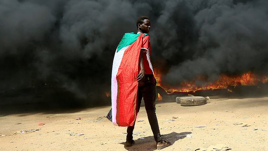 A person wearing a Sudan's flag stand in front of a burning pile of tyres during a protest against prospect of military rule in Khartoum, Sudan. Representative image. Credit: Reuters File Photo
