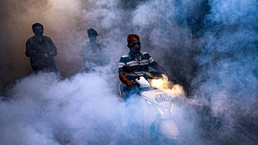 People walk amidst smoke as South Delhi Municipal Corporation (SDMC) workers fumigates an area to prevent mosquitos from breeding in New Delhi. Credit: AFP Photo