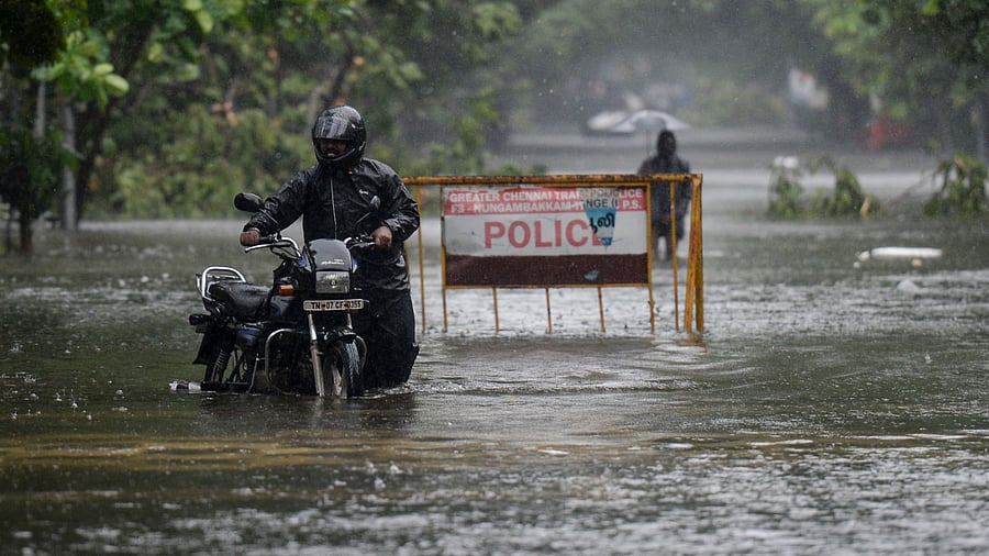 A man pushes his motorbike along a waterlogged street during a heavy monsoon rainfall in Chennai. Credit: AFP Photo