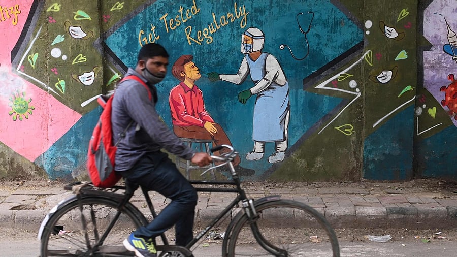 A cyclist rides past a mural depicting a health worker conducting Covid-19 coronavirus testing in New Delhi on November 6, 2021. Credit: AFP Photo