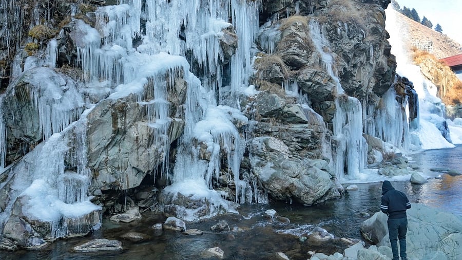 Visitors seen next to a frozen waterfall at Drung area of Baramulla district in Jammu and Kashmir. Credit: IANS Photo