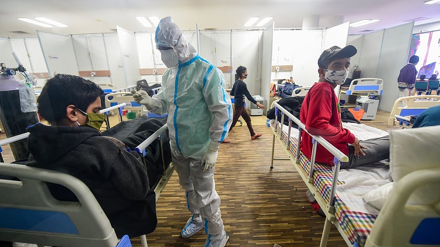 A health worker checks temperature of a Covid-19 infected patient inside a Covid care centre of the Commonwealth Games (CWG) village, in New Delhi. Credit: PTI File Photo