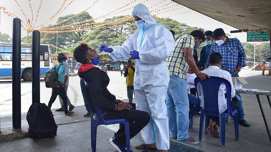 A health worker collects swab sample of a passenger for Covid-19 test at K R Market, during the weekend curfew imposed by the Karnataka government to curb the spread of Covid-19, in Bengaluru, Sunday. Credit: PTI Photo