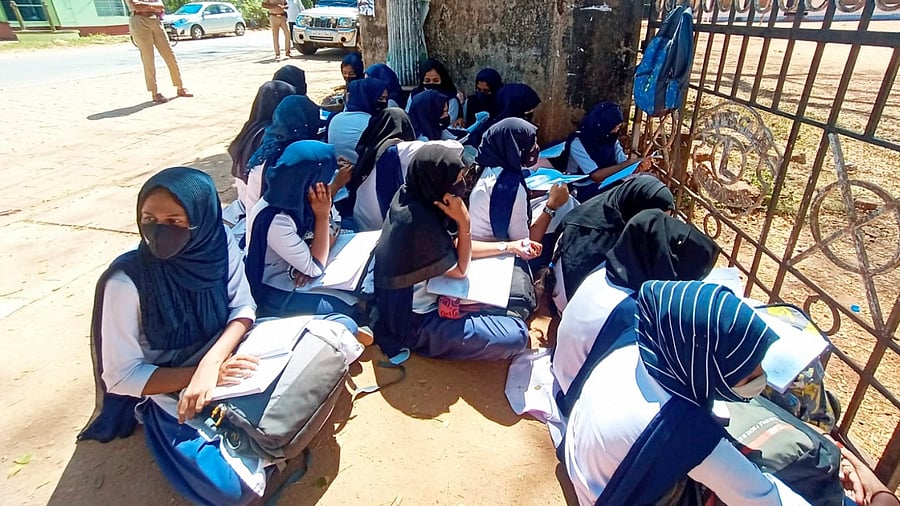 Students wearing hijab sit outside their school as the school authorities denied entry for wearing a hijab or scarf. Credit: PTI Photo
