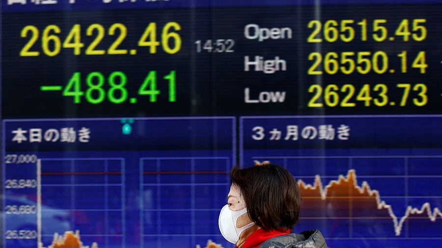 A woman wearing a protective mask, amid the coronavirus disease (COVID-19) outbreak, walks past an electronic board displaying Japan's Nikkei index outside a brokerage in Tokyo. Credit: Reuters Photo