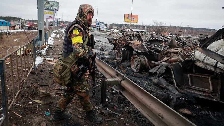 An armed man stands by the remains of a Russian military vehicle in Bucha, close to the capital Kyiv, Ukraine. Credit: AP/PTI Photo