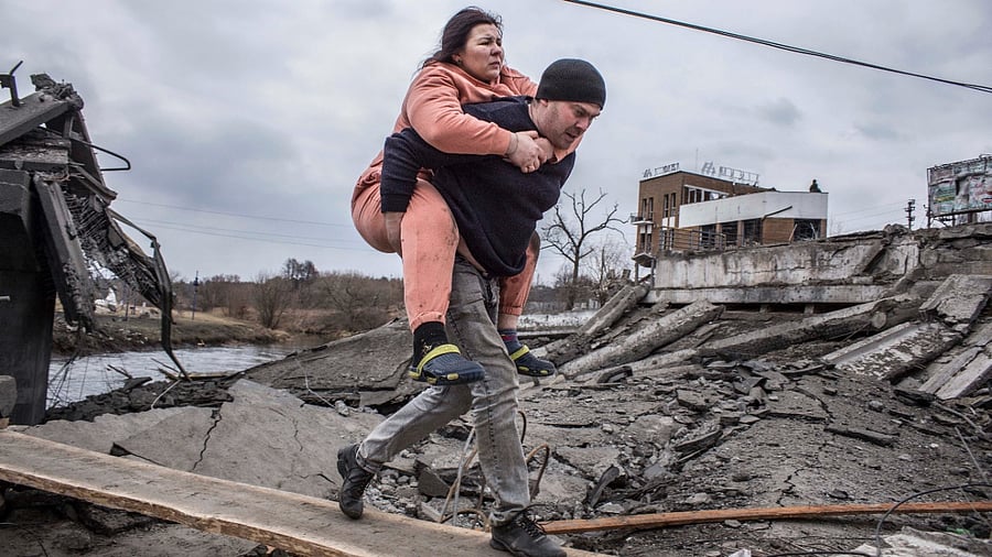 A man carries a woman as they cross an improvised path while fleeing the town of Irpin, Ukraine. Credit: AP/PTI photo
