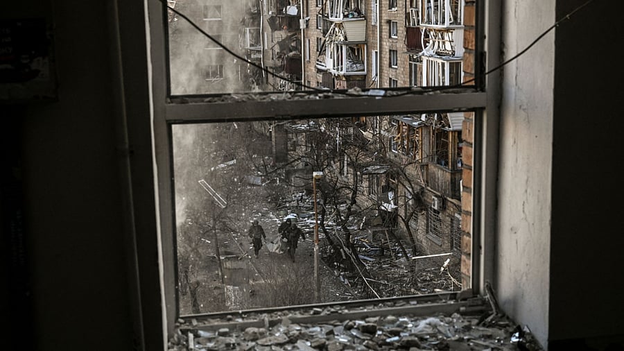 Ukranian servicemen are seen through a building window as they carry the remains of a missile after shelling in a residential area in Kyiv. Credit: AFP Photo