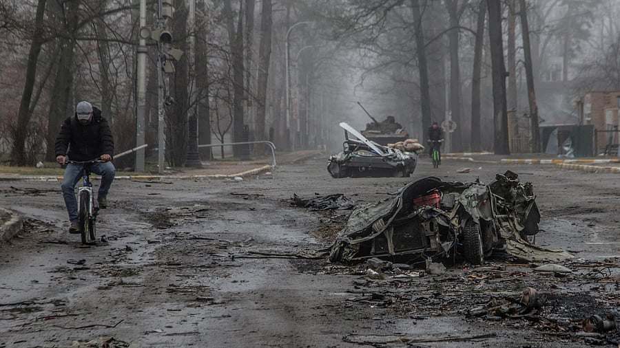Local residents ride bicycles past flattened civilian cars in Bucha. Credit: Reuters Photo