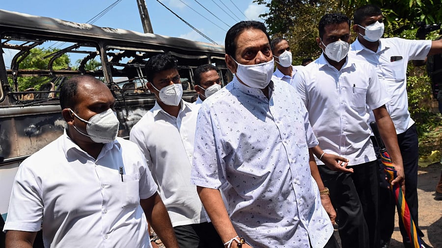 Sri Lanka's prime minister Mahinda Rajapaksa (C) is escorted past a burnt-out bus near Sri Lanka's President Gotabaya Rajapaksa's home in Colombo. Credit: AFP Photo