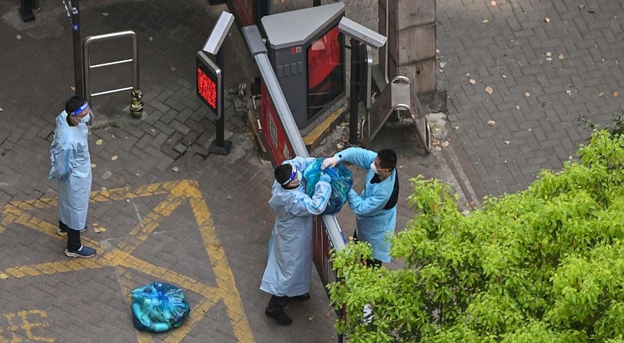 A guard, wearing personal protective gear, receives goods from a delivery worker in a compound during a COVID-19 lockdown in the Jing'an district in Shanghai on April 8, 2022. Credit: RETAMAL / AFP