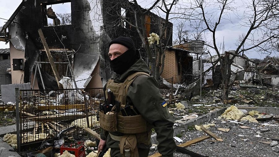 A member of the Ukrainian territorial defense forces walks in front of a destroyed house in Bohdanivka village, northeast of Kyiv. Credit: AFP