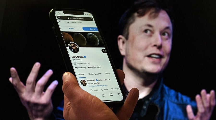 In this photo illustration, a phone screen displays the Twitter account of Elon Musk with a photo of him shown in the background. Credit: AFP