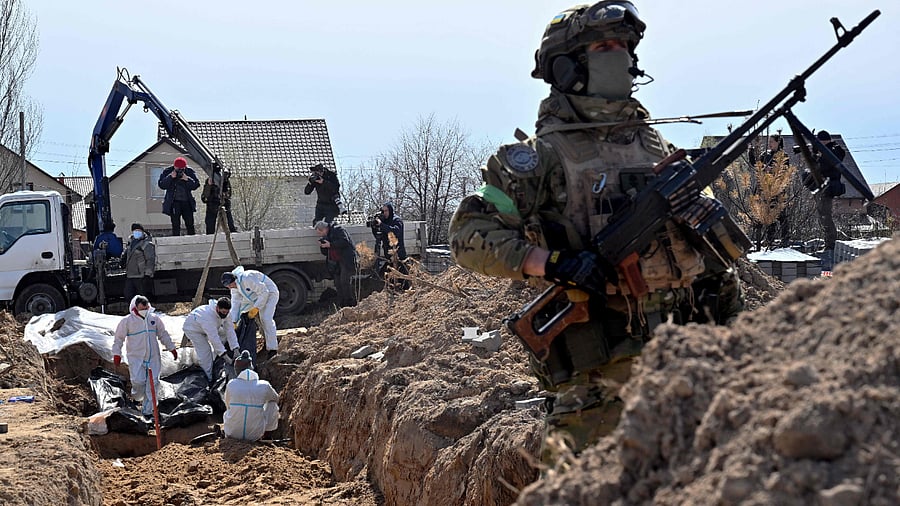 A Ukrainian serviceman looks on as workers exhume bodies from a mass grave in Bucha. Credit: AFP Photo