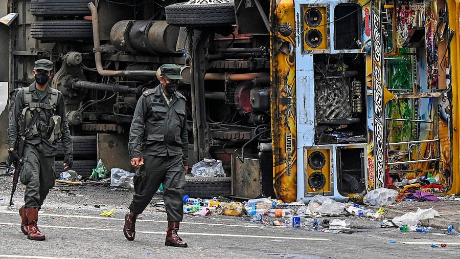 Security personnel walk past a burned vehicle along a road, a day after they were torched by protesters in Colombo. Credit: AFP Photo