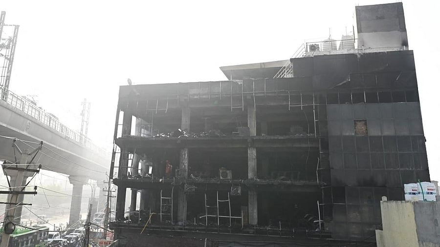 People watch from the street as National Disaster Response Force members and firefighters inspect a commercial building a day after a fire broke out in New Delhi. Credit: AFP Photo