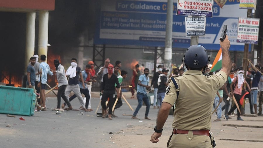 A policeman fires a gun during a protest against 'Agnipath scheme' for recruiting personnel for armed forces, in Patna. Credit: Reuters Photo